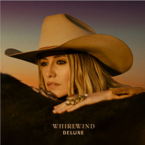 A woman wearing a light beige cowboy hat with a dark brown band.