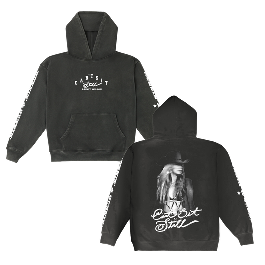 Black hoodie featuring a white graphic print of lainey wilson and the text ’can’t sit still’ on both front and back, with star patterns along the sleeves.