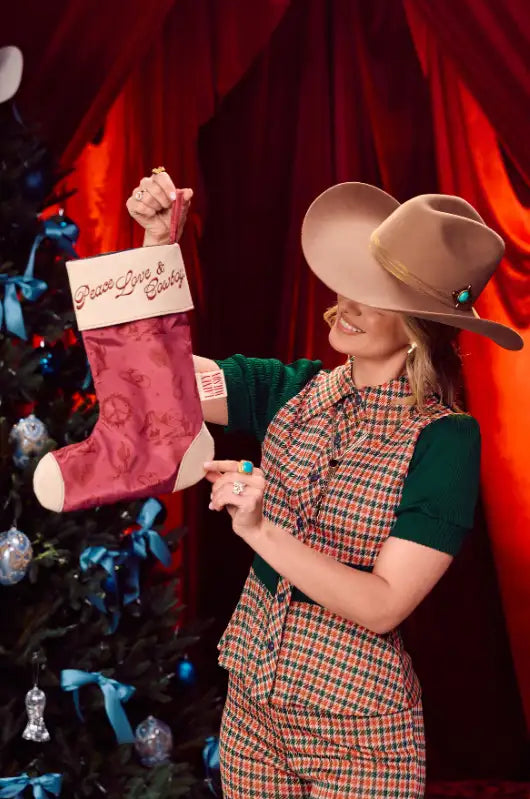 A festive pink satin christmas stocking with a cream-colored cuff embroidered with ’peace love & gratitude’ in gold thread.