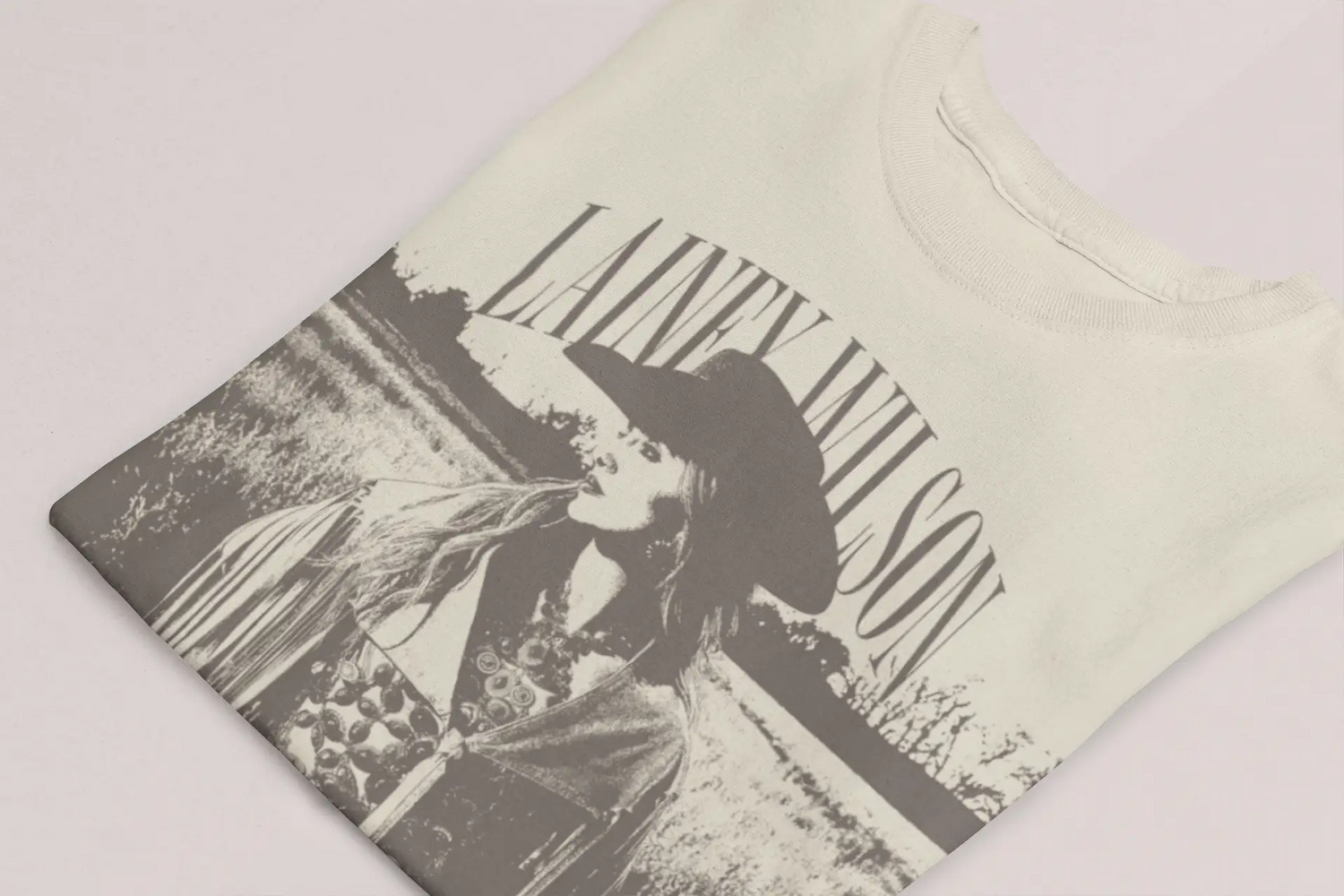Off-white cotton t-shirt featuring a black-and-gray graphic print of lainey wilson in a wide-brimmed hat with her name arched above.