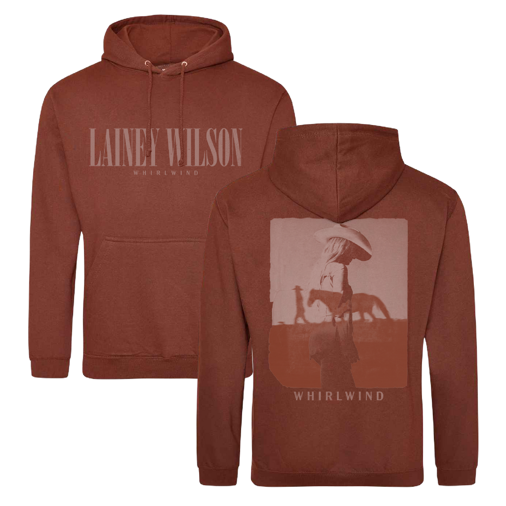 Rust-colored hoodie featuring ’lainey wilson’ and ’whirlwind’ branding with a graphic of a figure in a hat walking beside a horse on the back.